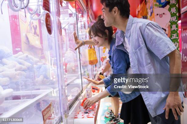 happy couples playing catch a doll - claw machine stock pictures, royalty-free photos & images