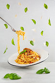Eating Italian pasta with bolognese meat and tomato sauce. Floating basil leaves and peace of parmesan cheese. Dynamic photo with levitation. Light grey background.