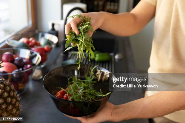 a young man prepares a vegetable salad in his kitchen. - roquette photos et images de collection