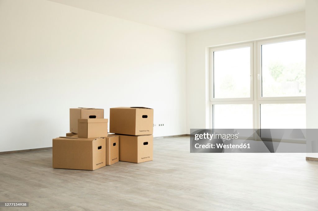 Cardboard boxes on hardwood floor against white wall in new house