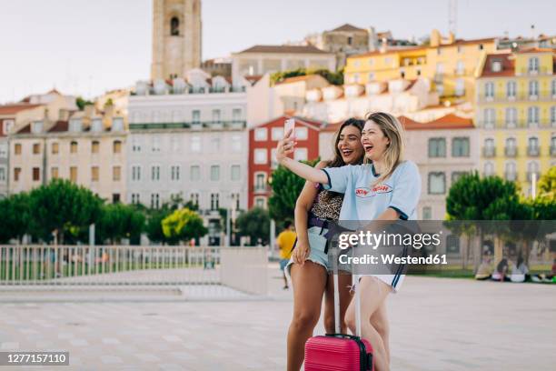 cheerful tourist taking selfie with female friend while standing on footpath in city - lisbon tourist stock pictures, royalty-free photos & images