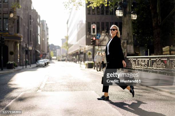 fashionable businesswoman crossing street in city - gehen stock-fotos und bilder