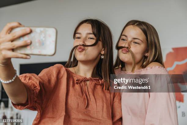 friends making fake mustache with hair while taking selfie at home - girl friends foto e immagini stock