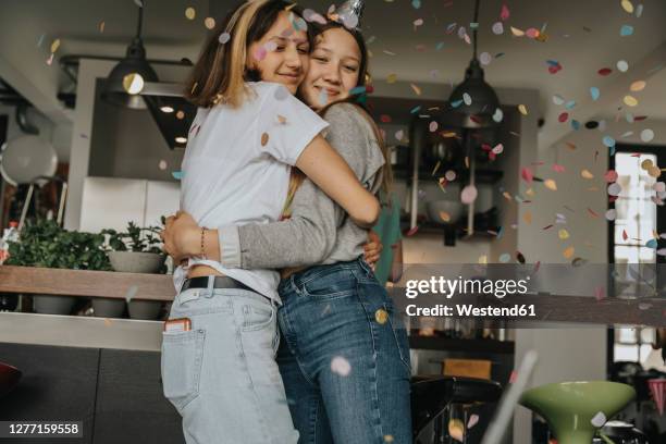 loving teenage friends embracing while standing in birthday party at home - happy moment stock-fotos und bilder