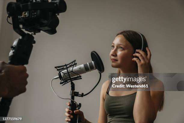 teenage girl looking at camera while singing over microphone against wall in studio - film crew studio stock pictures, royalty-free photos & images