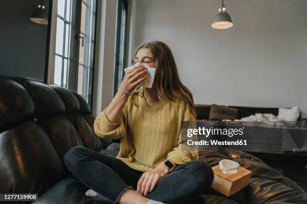 girl blowing nose while relaxing on coach at home - allergie stockfoto's en -beelden