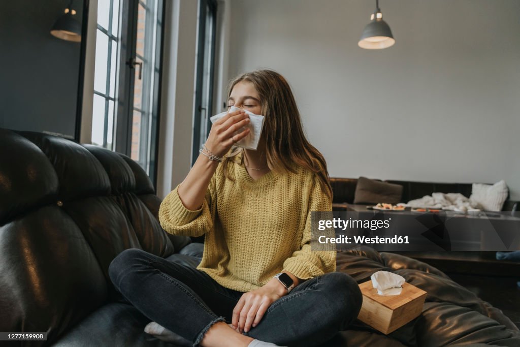 Girl blowing nose while relaxing on coach at home