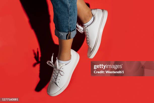 close-up of of female wearing sneakers while jumping against red background - laufschuhe stock-fotos und bilder