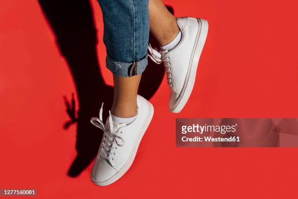 close-up of of female wearing sneakers while jumping against red background - footwear stock pictures, royalty-free photos & images