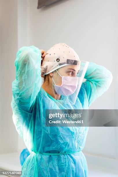 doctor in protective suit wearing face shield while standing at clinic - chirurgenkappe stock-fotos und bilder