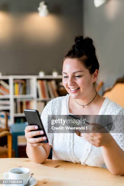 smiling voluptuous woman doing online shopping over mobile phone in coffee shop - chubby credit fotografías e imágenes de stock