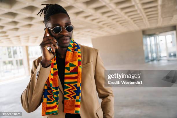 fashionable man wearing traditional kenete talking on phone while standing in building - black suit sunglasses stock pictures, royalty-free photos & images