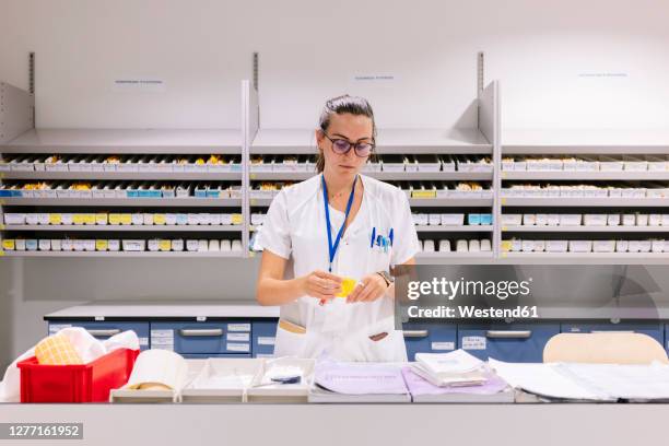 female pharmacist packing medicines on table while standing in storage room - preparing drug in hospital nurse stock pictures, royalty-free photos & images