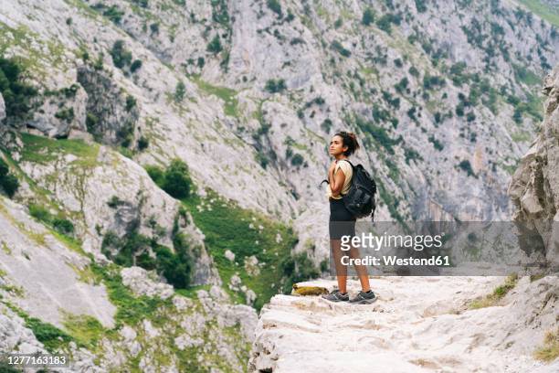 woman with backpack admiring view while standing on mountain path at ruta del cares, asturias, spain - picos de europa fotografías e imágenes de stock