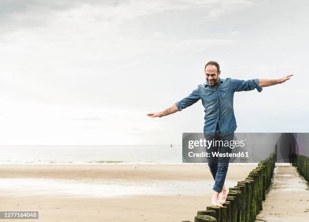carefree man with arms outstretched walking on wooden post at beach - homem 55 anos imagens e fotografias de stock