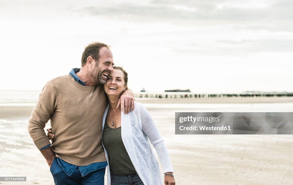 Cheerful man embracing woman while standing against sea during sunset