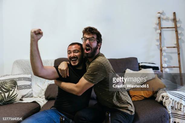 excited male spectators screaming while watching sports in living room - match sport fotografías e imágenes de stock