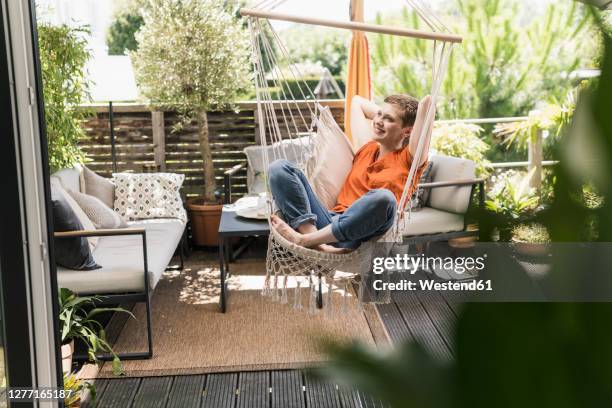 thoughtful woman with hands behind head swinging in porch seen through indoors - cushion stock-fotos und bilder