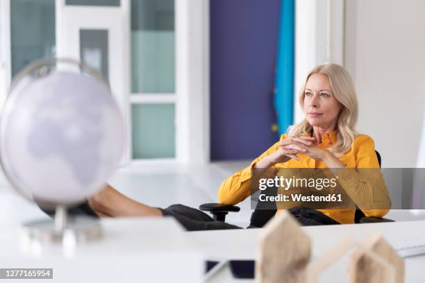 thoughtful businesswoman with hands clasped sitting on chair in home office - tisch betrachten stock-fotos und bilder