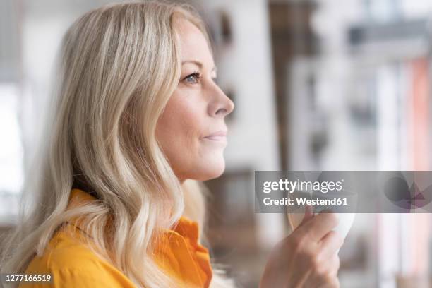 close-up of thoughtful businesswoman holding coffee cup in home office seen through window - head shot close looking stockfoto's en -beelden