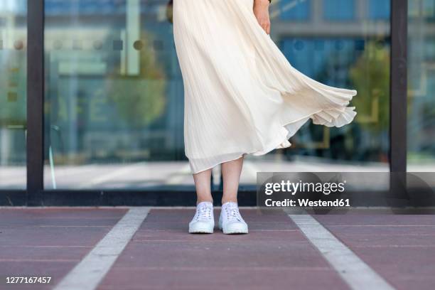 legs of senior woman standing against glass window on footpath - windy skirt - fotografias e filmes do acervo