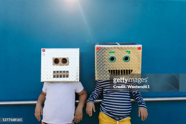friends wearing robot costumes made of boxes while standing against blue wall - robot costume stock-fotos und bilder