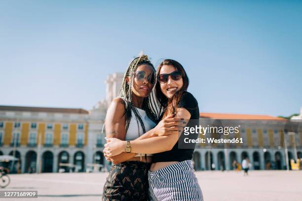 women embracing each other at praca do comercio against clear sky, lisbon, portugal - comercio stock-fotos und bilder