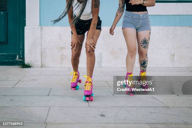 low section of friends skating on footpath against wall in city - patín de ruedas fotografías e imágenes de stock