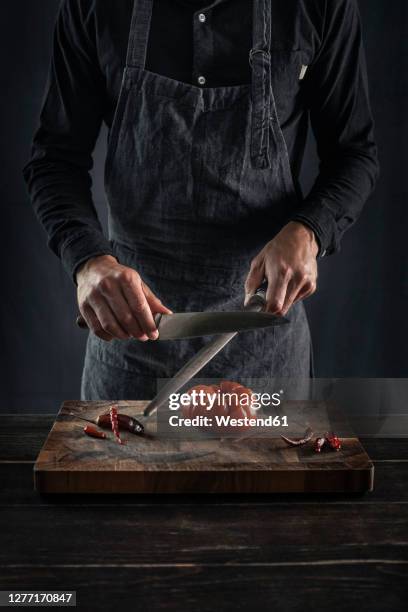 man sharping knife while standing at table - kochmesser stock-fotos und bilder