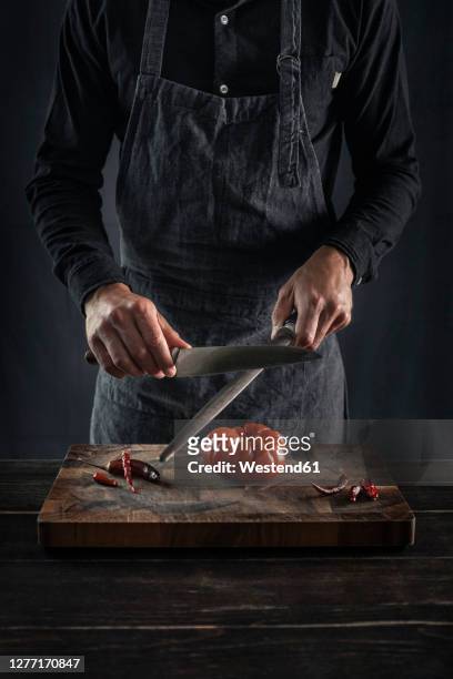 man sharping knife while standing at table - afilado fotografías e imágenes de stock