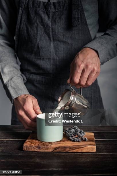 man pouring milk in cup while standing at table - steamed stock-fotos und bilder