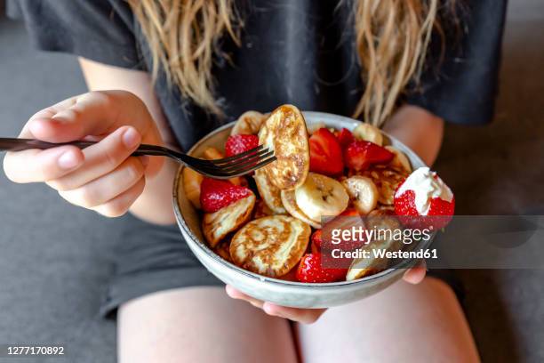 mid section of teenage girl eating bowl of mini pancakes with strawberries and bananas - petite teen girl stock-fotos und bilder
