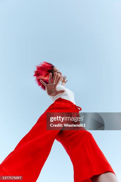 young woman doing stop gesture while standing against blue sky - red pants stock-fotos und bilder