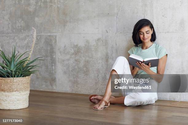 businesswoman reading book while relaxing on hardwood floor against wall in office - arab businesswoman with books stock-fotos und bilder