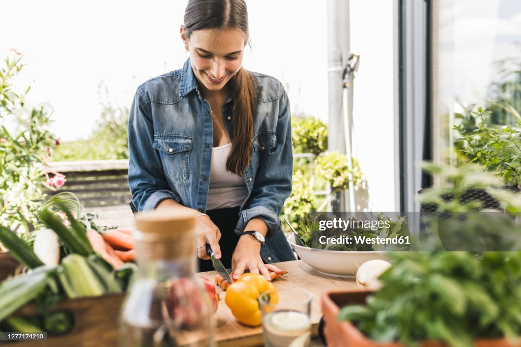 Smiling young woman chopping vegetables on cutting board in yard