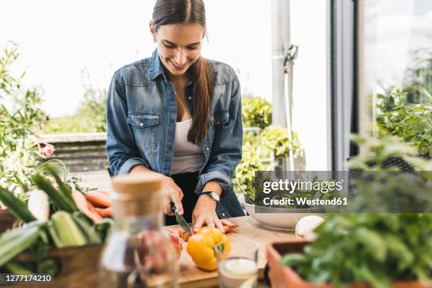 smiling young woman chopping vegetables on cutting board in yard - cutting long hair stock pictures, royalty-free photos & images