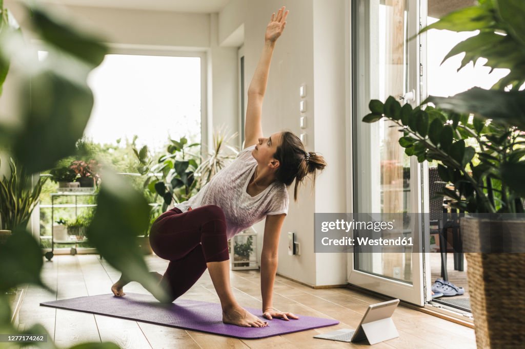 Young woman with digital tablet exercising on mat at home