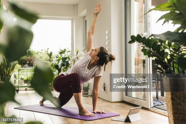 young woman with digital tablet exercising on mat at home - flessibilità foto e immagini stock