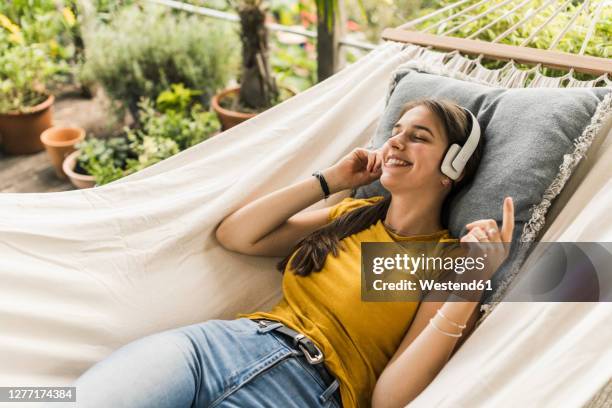 woman with eyes closed listening music through headphones while relaxing on hammock in yard - garden hammock stock pictures, royalty-free photos & images