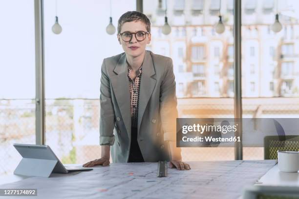 portrait of confident businesswoman leaning on desk in office - lead stock-fotos und bilder