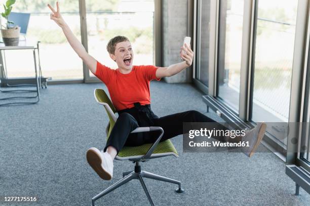 carefree businesswoman using smartphone in office - peace sign gesture stock-fotos und bilder