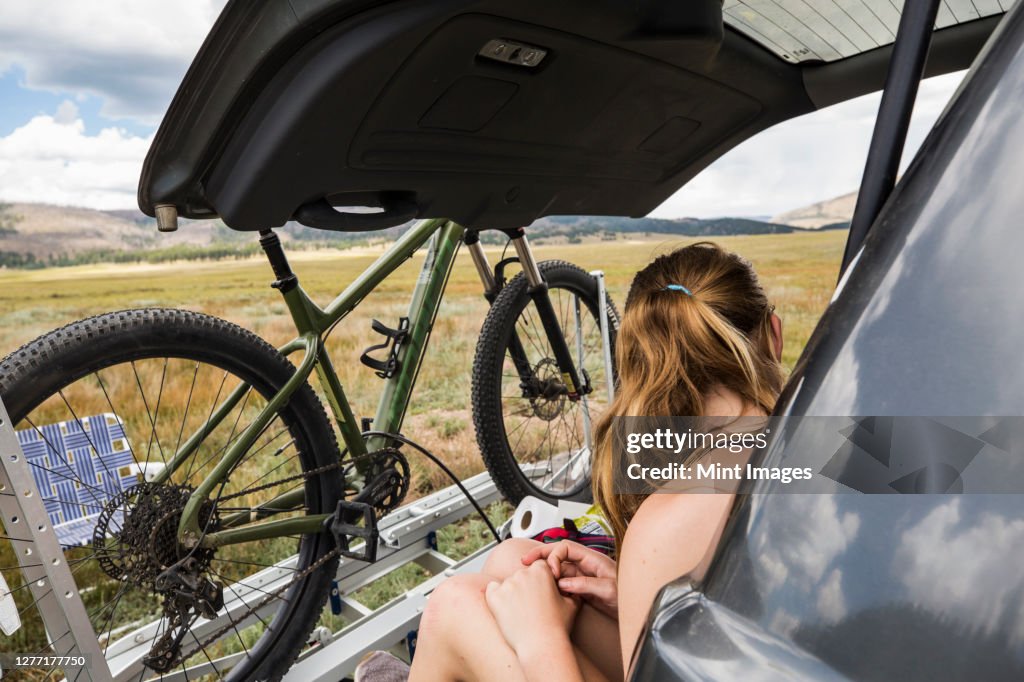 Teenage girl sitting on the tailgate of an SUV looking at vista