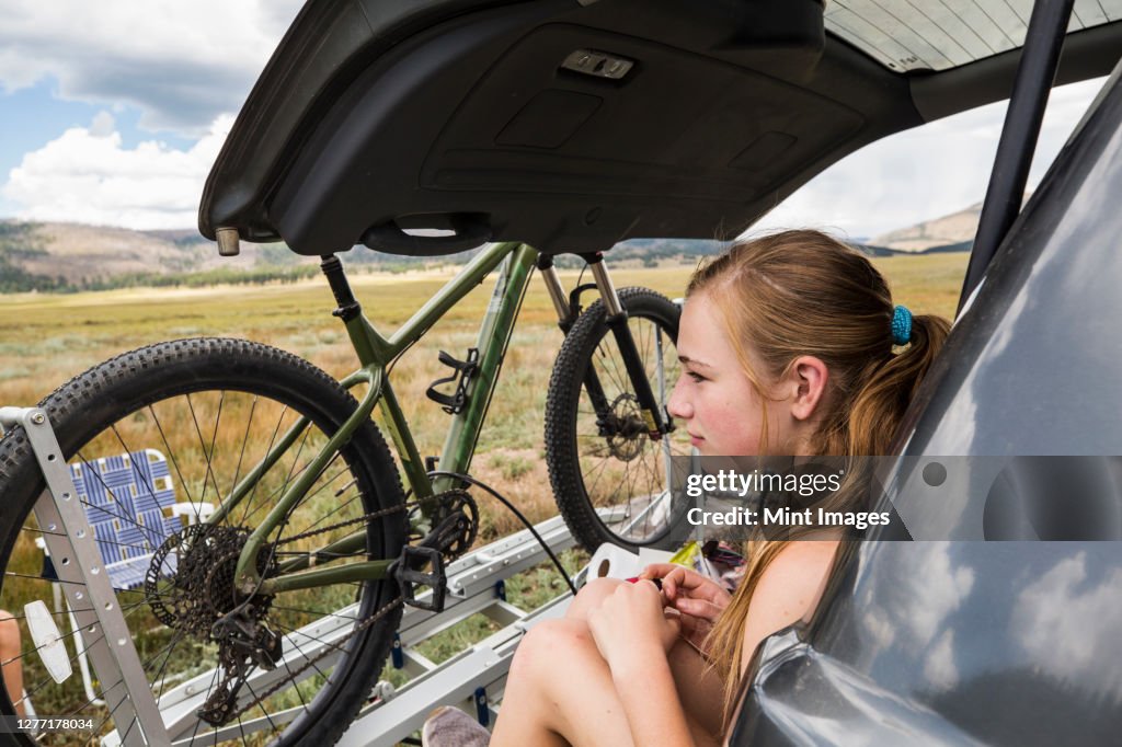 Teenage girl sitting on the tailgate of an SUV looking at vista