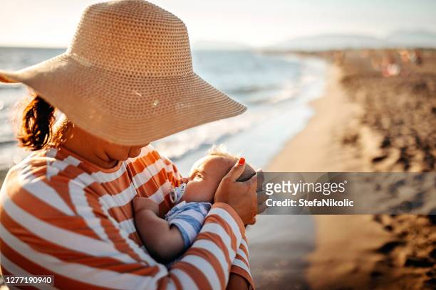 madre sosteniendo bebé cerca del mar - mothers day beach fotografías e imágenes de stock