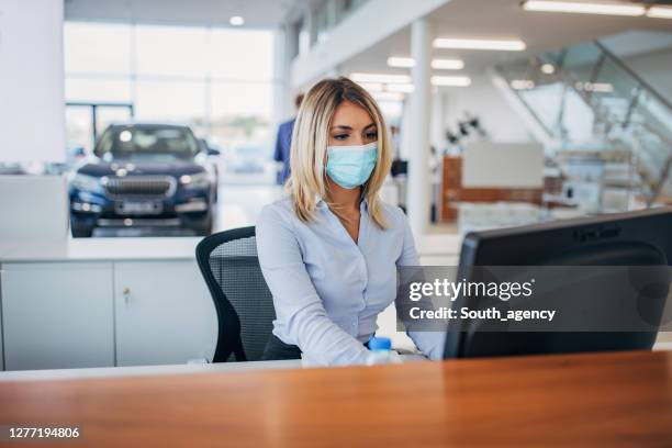 one female car dealer with protective face mask working on computer in showroom - car dealership covid stock pictures, royalty-free photos & images