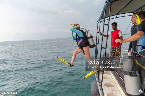 een vrouw - duiker die een duikpak en aqualung draagt, springt aan de oceaan van een boot. - aqualung diving equipment stockfoto's en -beelden