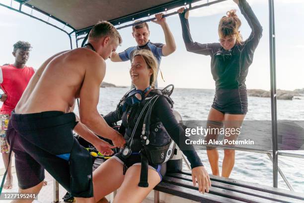 a man - diving instructor and personal trainer is helping to adjust diving equipment for a young happy woman aboard of a boat going to the ocean, with a company of other divers. - competitive diving stock pictures, royalty-free photos & images