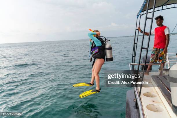 una mujer - buceador con un traje de buceo y aqualung, está saltando al océano desde un barco. - aqualung diving equipment fotografías e imágenes de stock