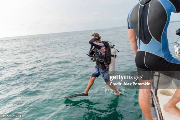 un hombre, el buzo con traje de buceo y aqualung, está saltando al océano desde un barco. - aqualung diving equipment fotografías e imágenes de stock