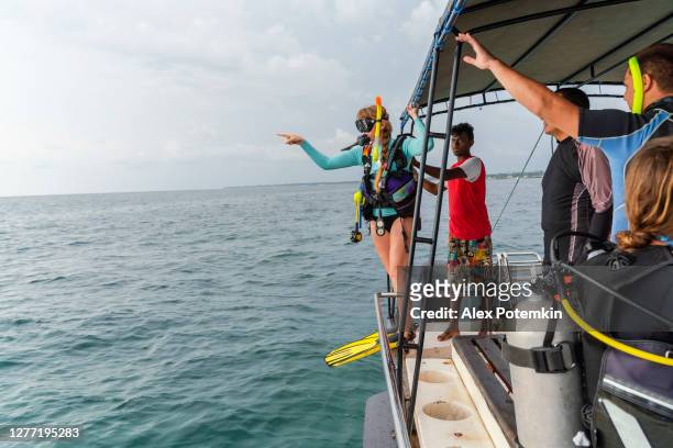 een vrouw - duiker die een duikpak en aqualung draagt, bereidt zich voor om aan de oceaan van een boot te springen. - aqualung diving equipment stockfoto's en -beelden